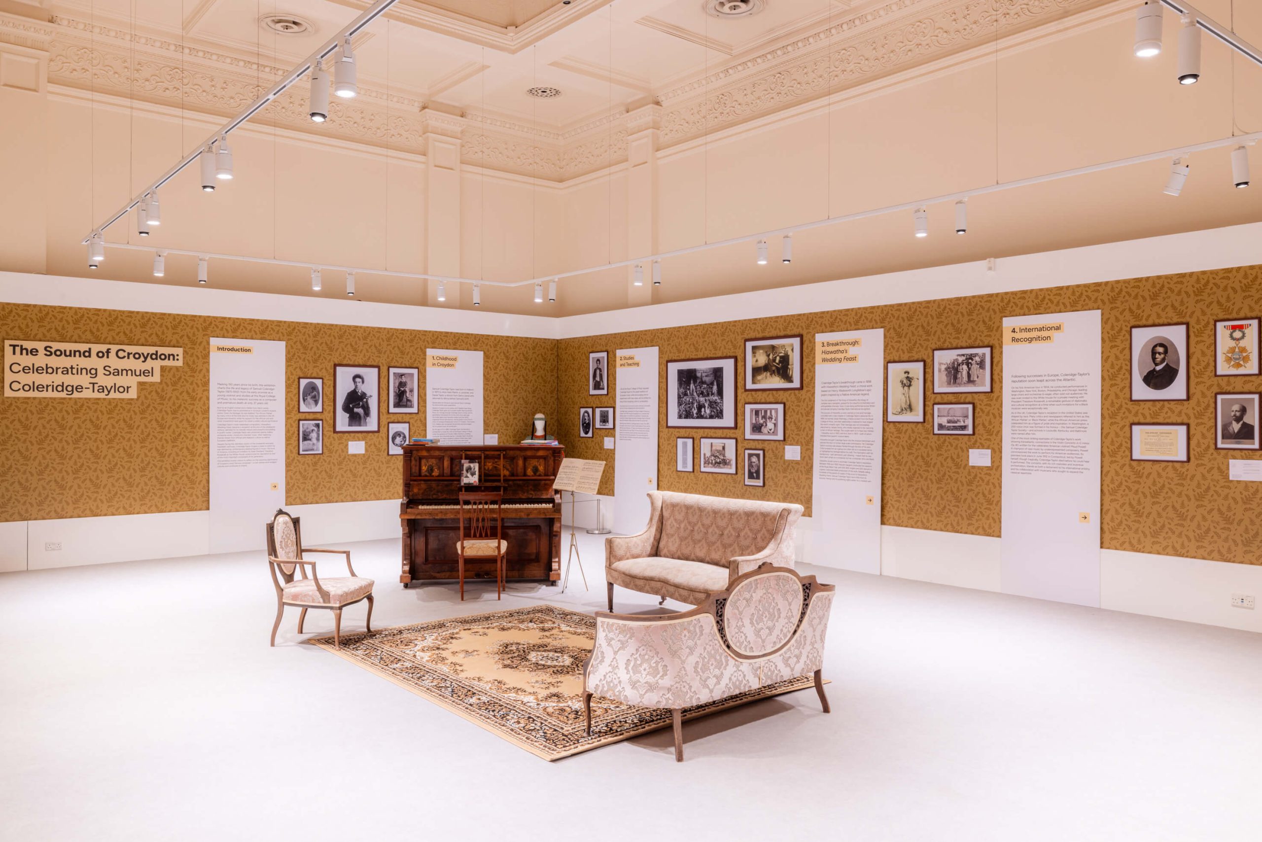 Museum exhibition titled “The Sound of Croydon: Celebrating Samuel Coleridge-Taylor,” styled like a Victorian sitting room with a piano, upholstered seating, and display panels of photographs and text.