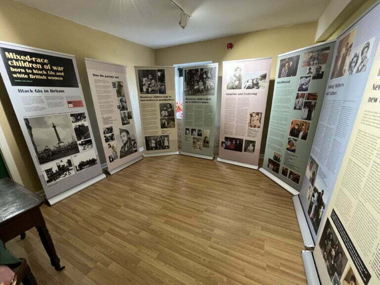 Nine floor to ceiling high posters that make up the Brown Babies of WW2 travelling exhibition displayed in a room.