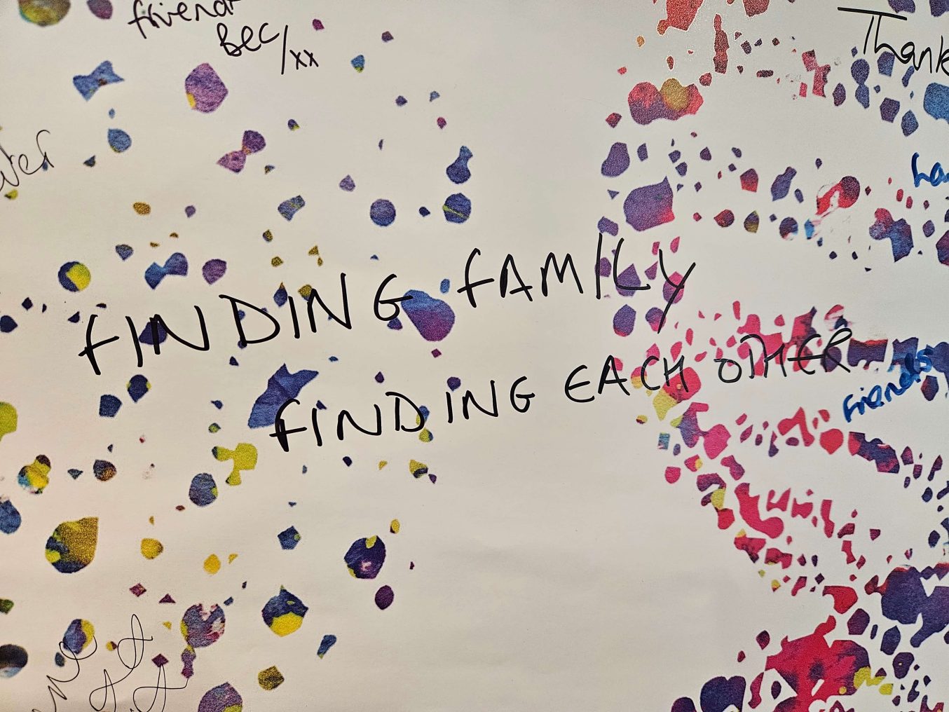 Handwritten text reading “Finding family, finding each other” surrounded by colourful paint splatters of a double helix and participant writing from The Mixed Museum's Brown Babies DNA project.