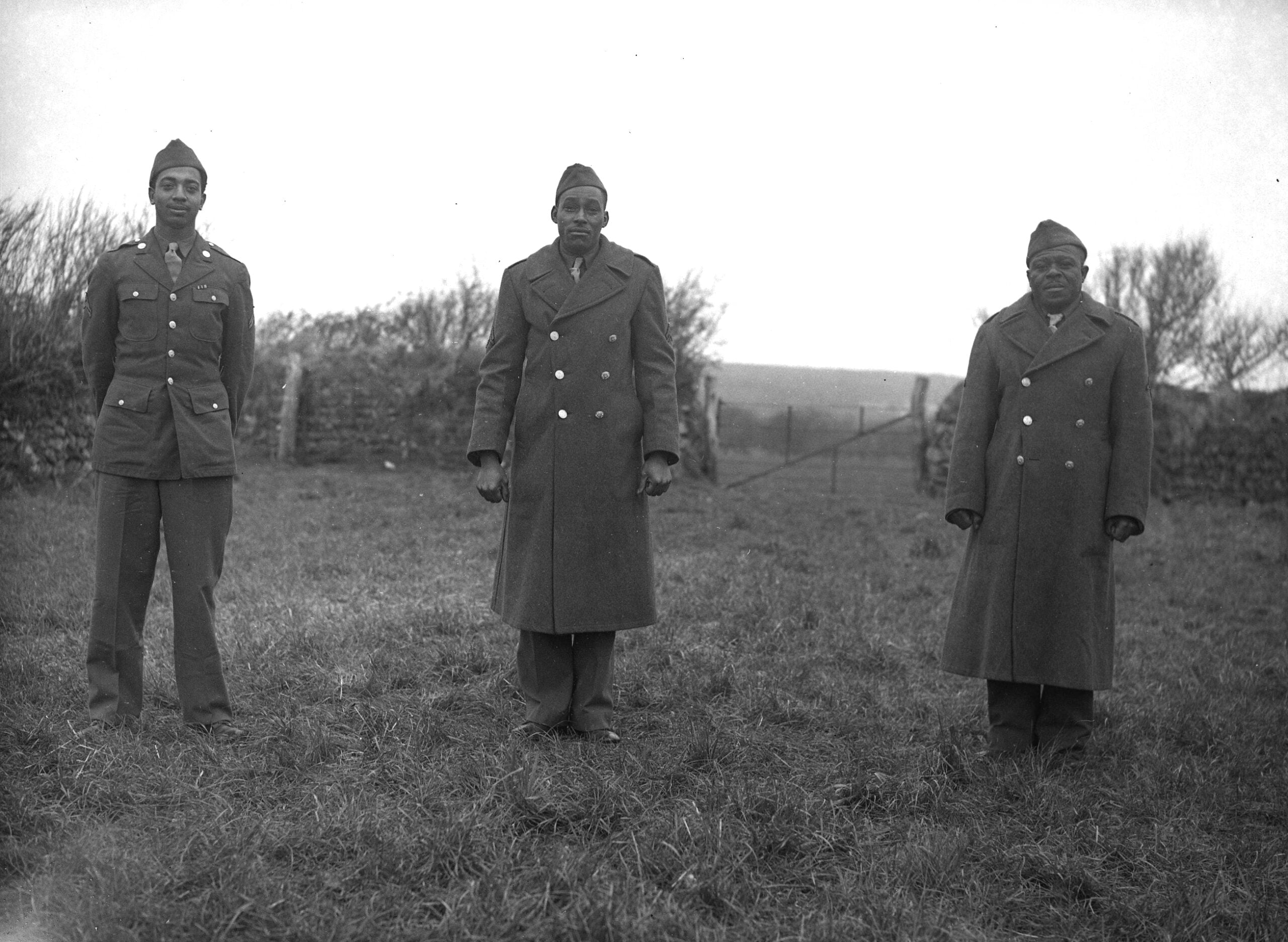 Three Black American world war two soliders standing in a field and looking at the camera.