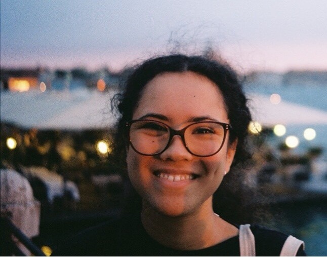 Photo of artist Amy Townsend-Lowcock smiling, wearing glasses, outdoors at dusk.