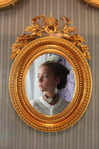 Image of a young mixed race girl in side profile. She is dressed in 18th century costume and the photograph is surrounded by a gilt frame.