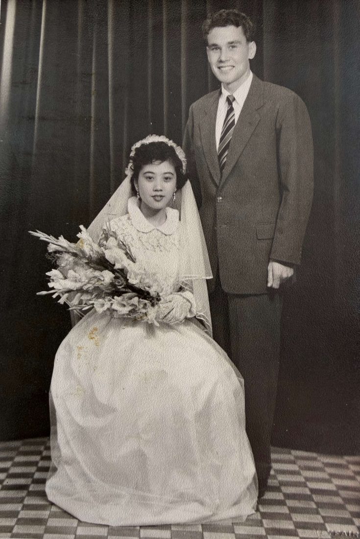 Black-and-white wedding portrait of a Allan O'Neill's Chinese mother in a traditional European style wedding gown and veil seated beside a his white British father in a suit, taken in Hong Kong in 1955.