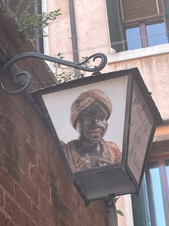 Hanging shop sign in Venice depicting a Black figure in a turban mounted on a building exterior.
