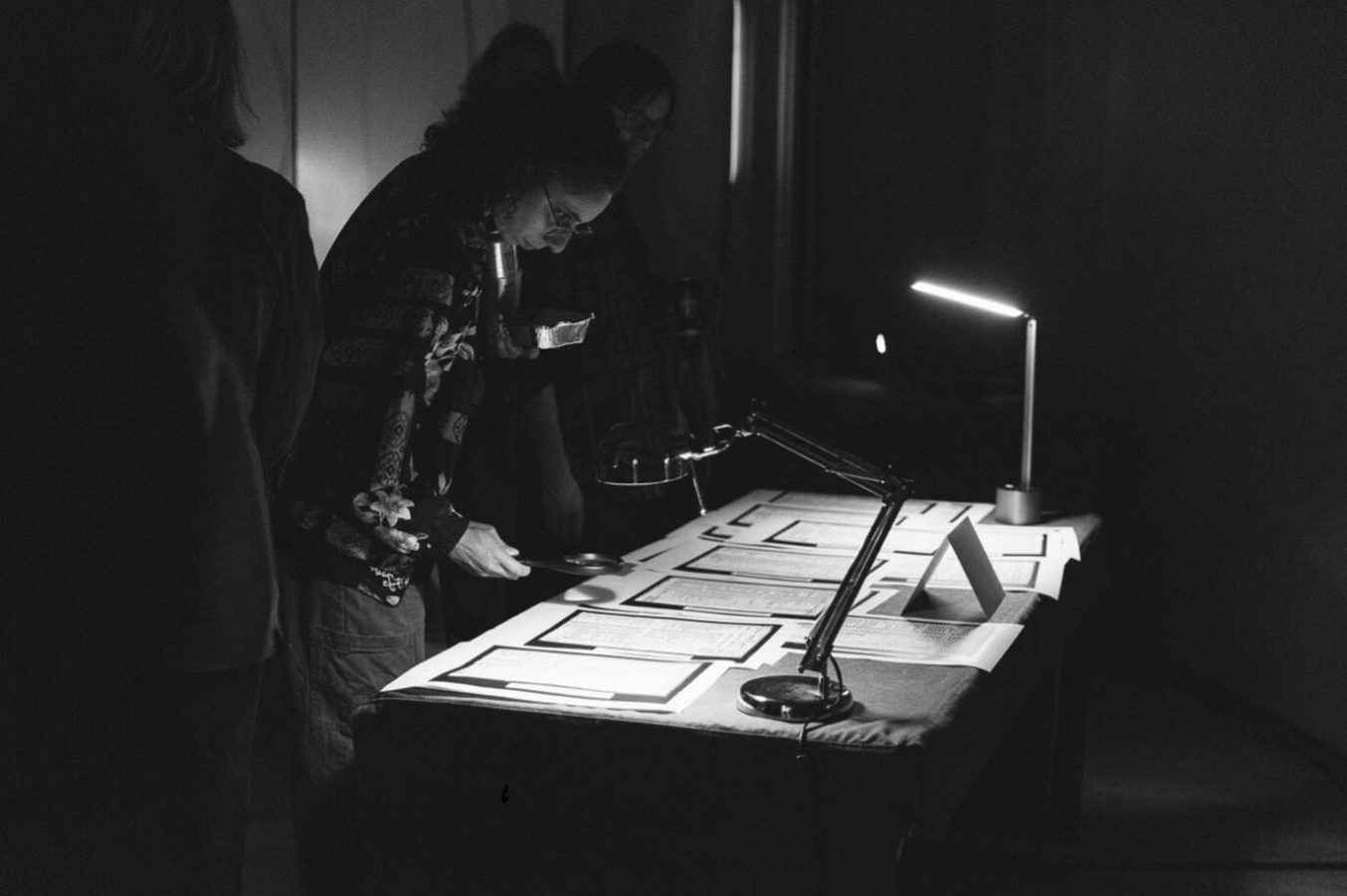 Visitor examines documents on a table under a desk lamp in a dimly lit pop-up exhibition at the Lowry.