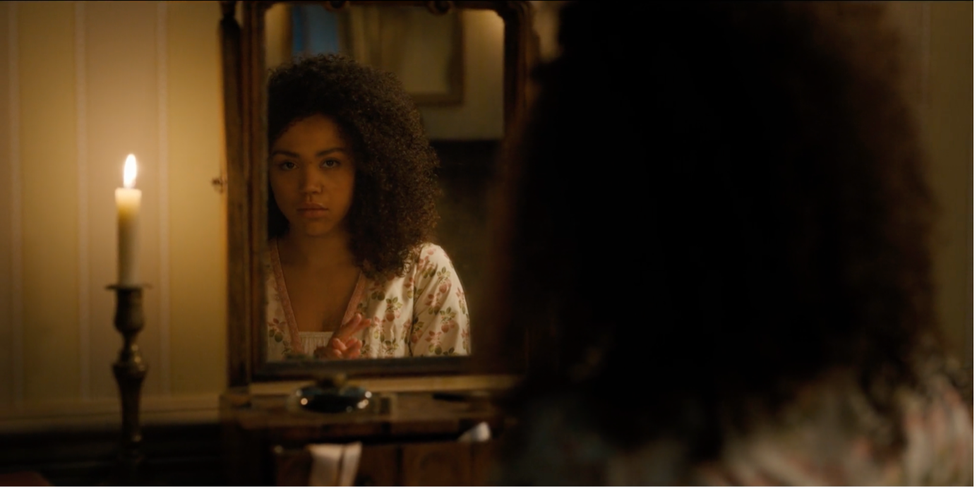 Bridgerton Character Marina Thompson looks at her reflection in a mirror by candlelight.