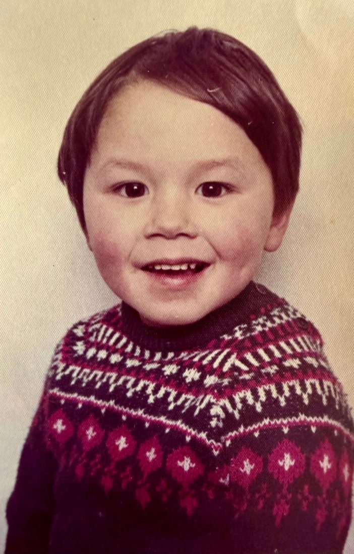 Studio portrait of Allan O'Neill as a young child wearing a patterned jumper and smiling happily at the camera
