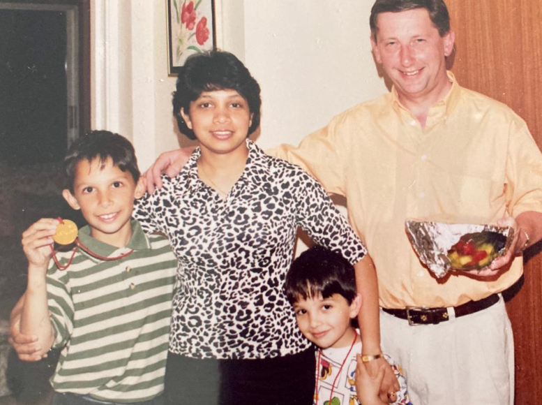 Family photograph of Lucas Fothergill as a child with his Sri Lankan mother, white British father and younger, brother at home, smiling at the camera with their arms around each other.