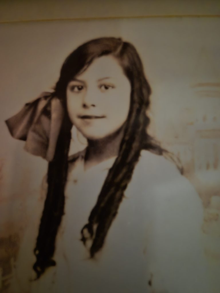 Sepia-toned portrait of Sarah Sadler's grandmother Maie Lillian Lung as a young girl, with long dark hair and a large bow, facing the camera.