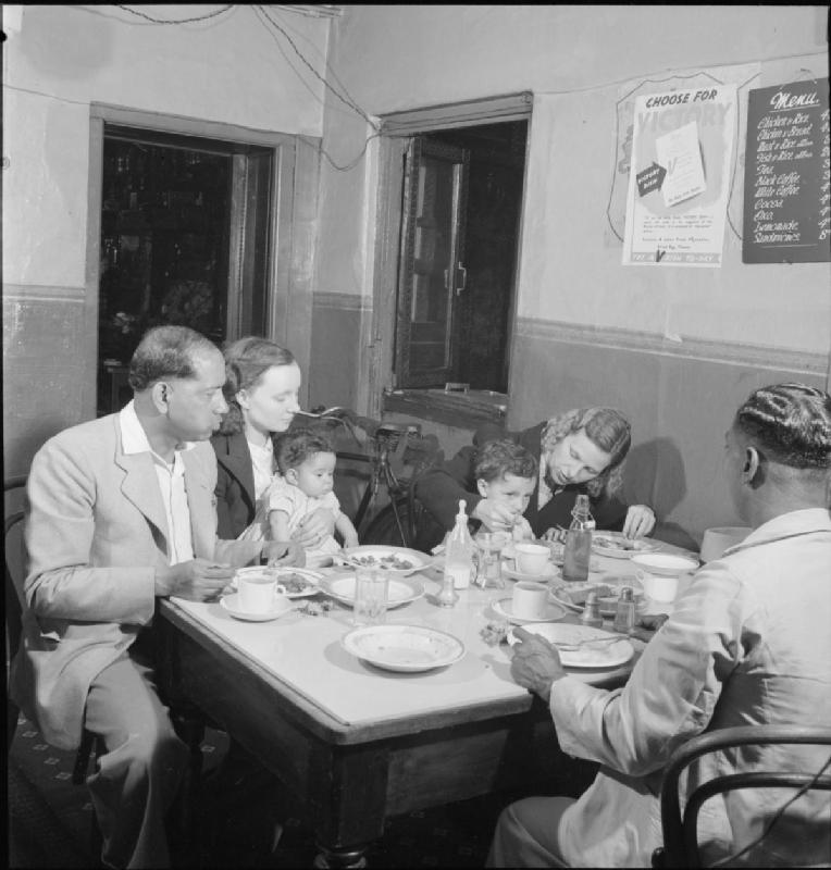 A photograph taken in 1943 by the Ministry of Education as part of its ‘Everyday Life in Butetown, Cardiff’ series. The accompanying caption reads ‘Visitors to Butetown for the opening of the new Mosque enjoy a meal at 'The Cairo' cafe. Left to right, they are: Abdul Aziz, from Calcutta, who runs a cafe in South Shields, Mrs Aziz and their daughter Joynob, Mrs Annie Nian, with her son Kenneth and Azin Ulla, a seaman from Bengal.’ Image: public domain, via the Imperial War Museums/Wikipedia