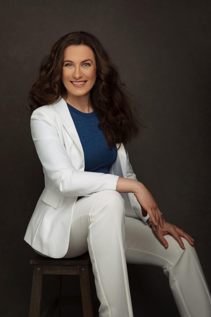 Sophie0032©LenkaJones RESIZED Photograph of Dr Sophie Kay seated on a chair, wearing a white suit and smiling at the camera.