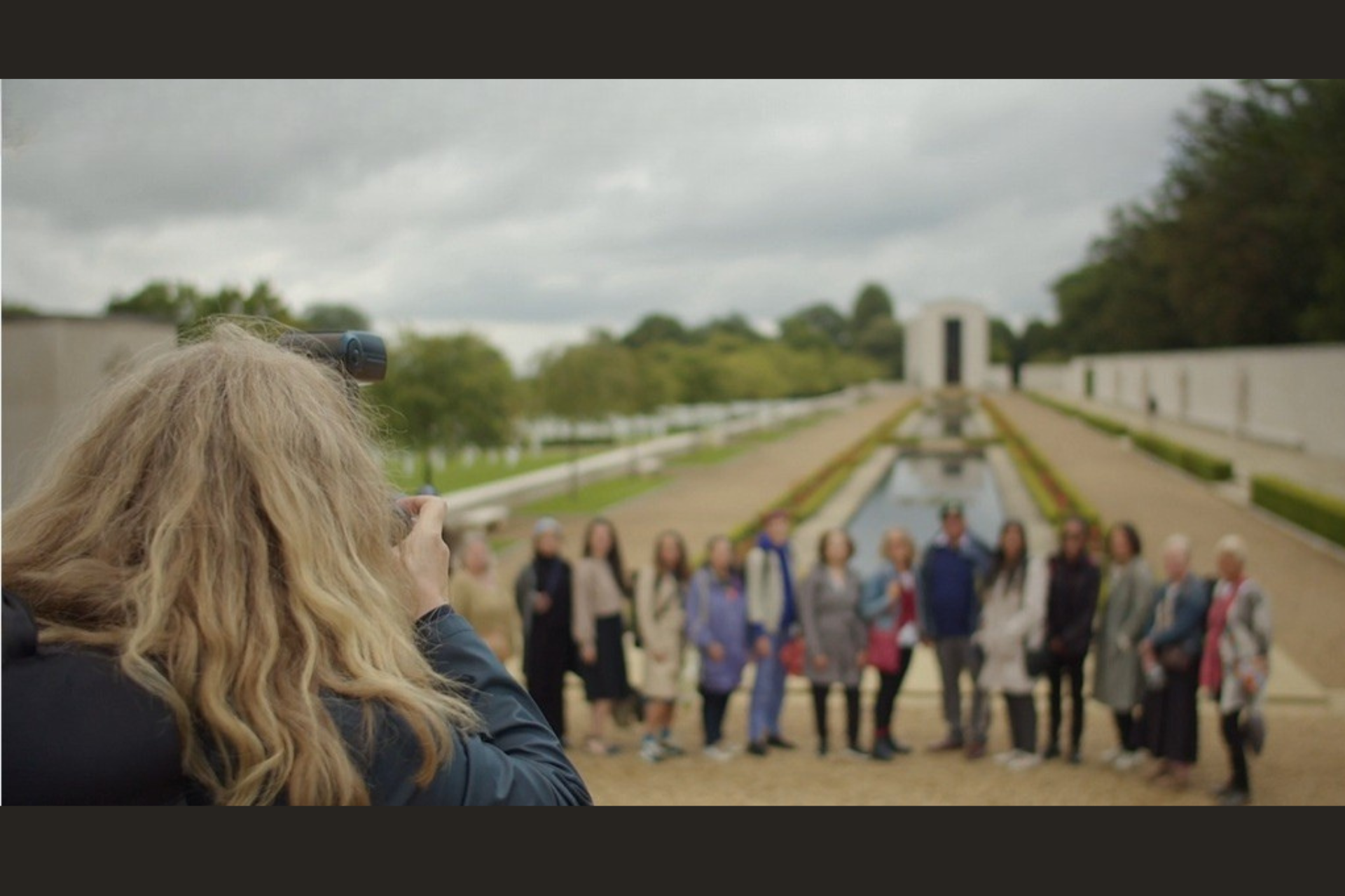 A still taken from behind of Susan Alexander photographing members of TMM's 'Brown Babies' DNA Histories group at the Cambridge American Cemetery.