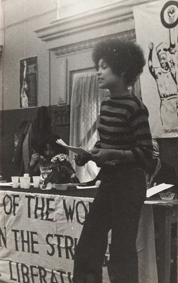 Sylvia Ome Erike presenting her paper on Black women and the State at the first National Black Women’s Conference in 1979 Image courtesy Stella Dadzie via Black Cultural Archives Sylvia Ome Erike speaks at the first National Black Women’s Conference in 1979, holding papers beside banners and seated attendees.