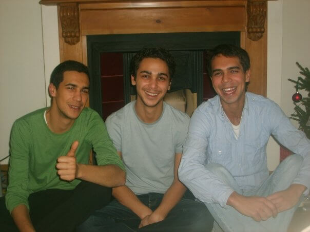Carl as a young man sitting with his brothers in front of a fireplace, all three smiling at the camera.