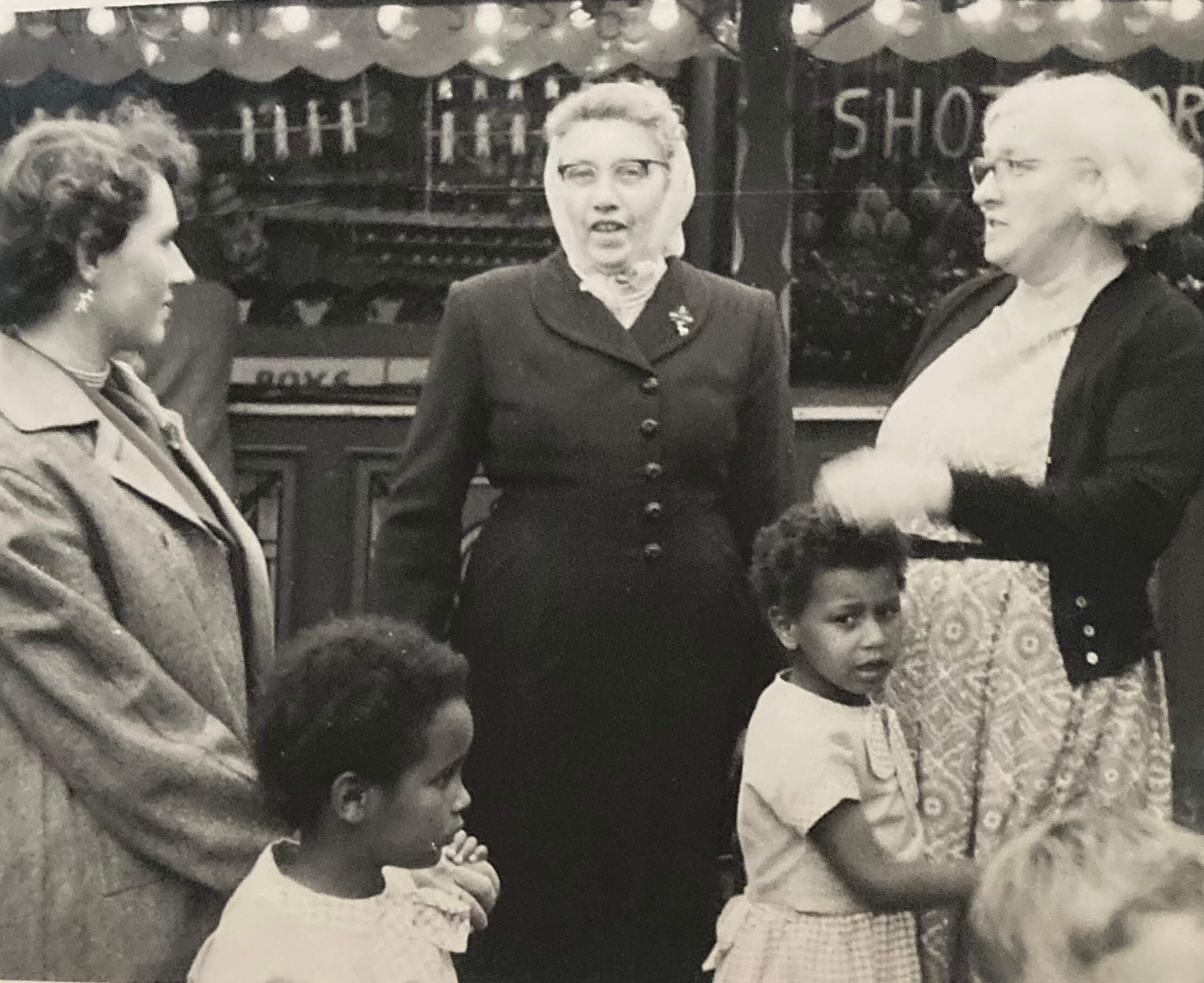 Black-and-white photograph of Tina Shingler and another child standing with her foster mother Mary and two women at a local fair.